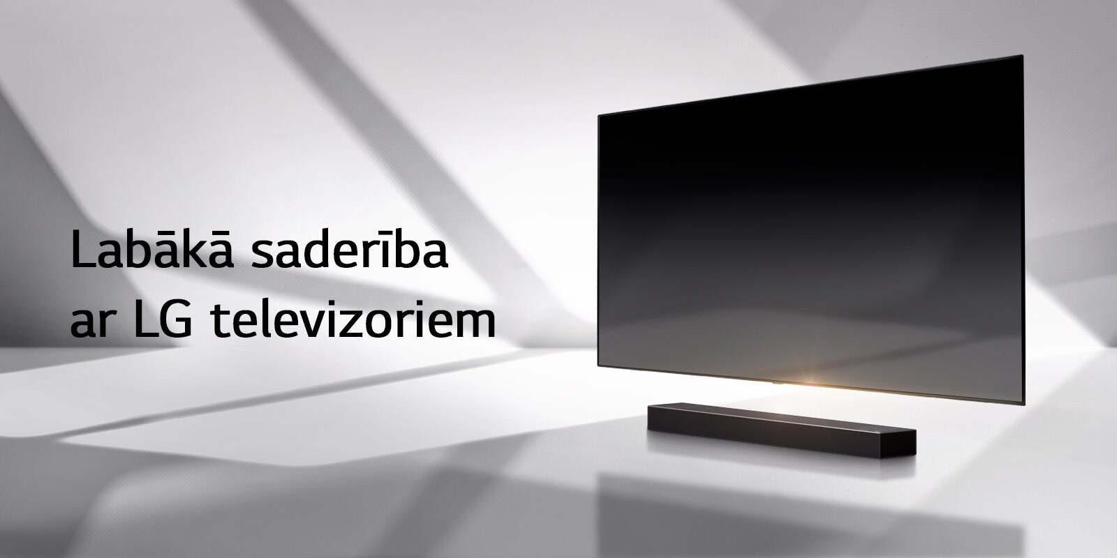 Skaņas josla un televizors novietoti uz baltas grīdas, un no ārpuses aiz tiem stiepjas ēna.