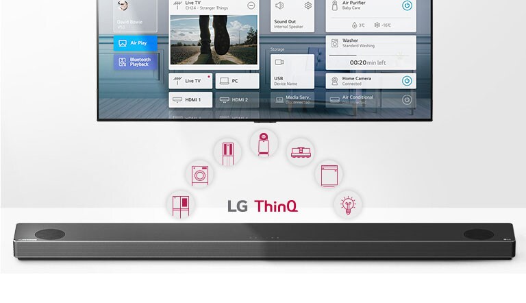 TV pie sienas. LG skaņas josla zem televizora. LG ThinQ logotips un iekārtu ikonas starp televizoru un LG skaņas joslu.
