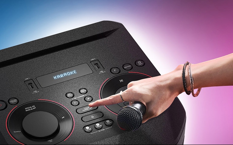 Roka ar mikrofonu cenšas nospiest balss noņēmēja pogu uz LG XBOOM.