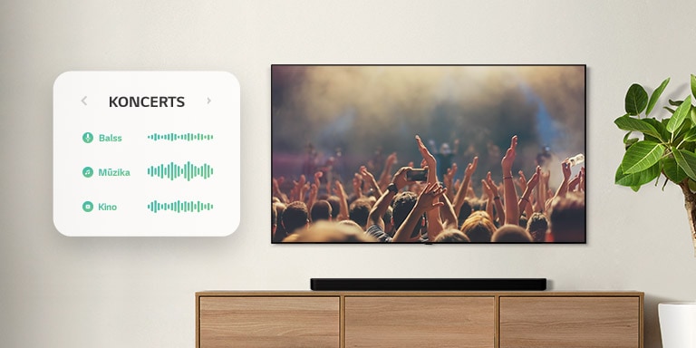 TV pie sienas. Televizorā redzami cilvēki, kas aplaudē koncertā, kanāls tiek pārslēgts uz filmu ainu ar pa mežu braucošu automašīnu, pēc tam kanāls tiek pārslēgts uz ziņām, un runā ziņu vadītājs. Tieši zem televizora uz smilškrāsas plaukta izvietota LG skaņas josla. (atskaņot video)