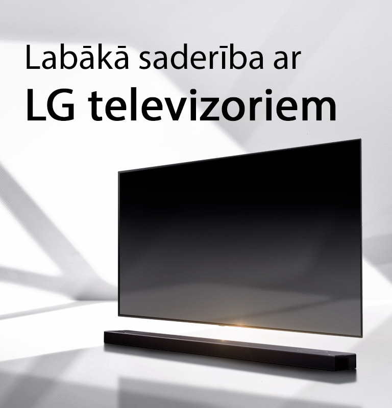 Skaņas josla un televizors novietoti uz baltas grīdas, un no ārpuses aiz tiem stiepjas ēna.