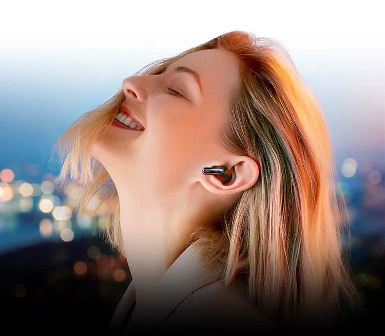 Aiz uzraksta “Atsvaidzini savu klausīšanos” sieviete ar TONE Free ausīs klausās mūziku naksnīgā pilsētā.