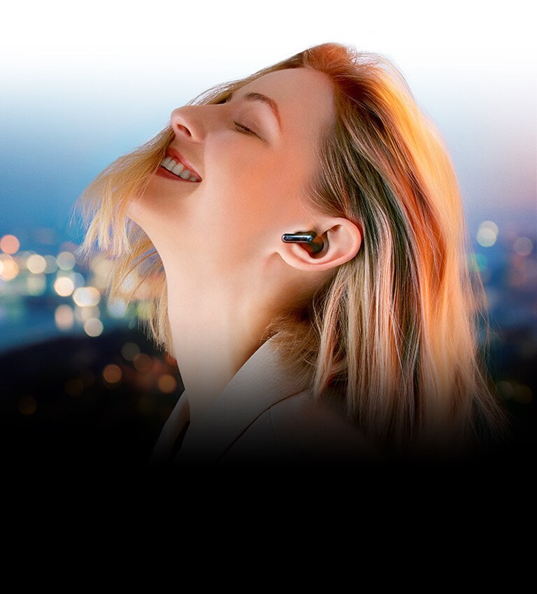 Aiz uzraksta “Atsvaidzini savu klausīšanos” sieviete ar TONE Free ausīs klausās mūziku naksnīgā pilsētā.