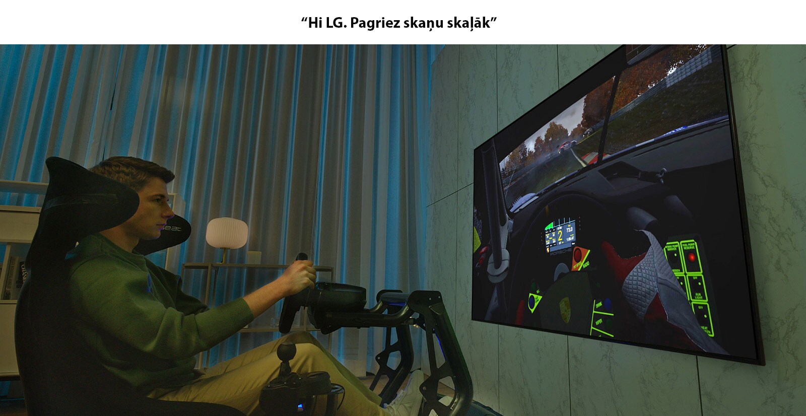 Vīrietis sēž sacīkšu krēslā pretī lielam televizoram un spēlē ātrumsacīkšu spēli.