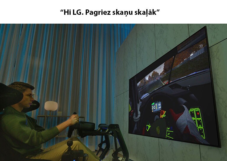 Vīrietis sēž sacīkšu krēslā pretī lielam televizoram un spēlē ātrumsacīkšu spēli.