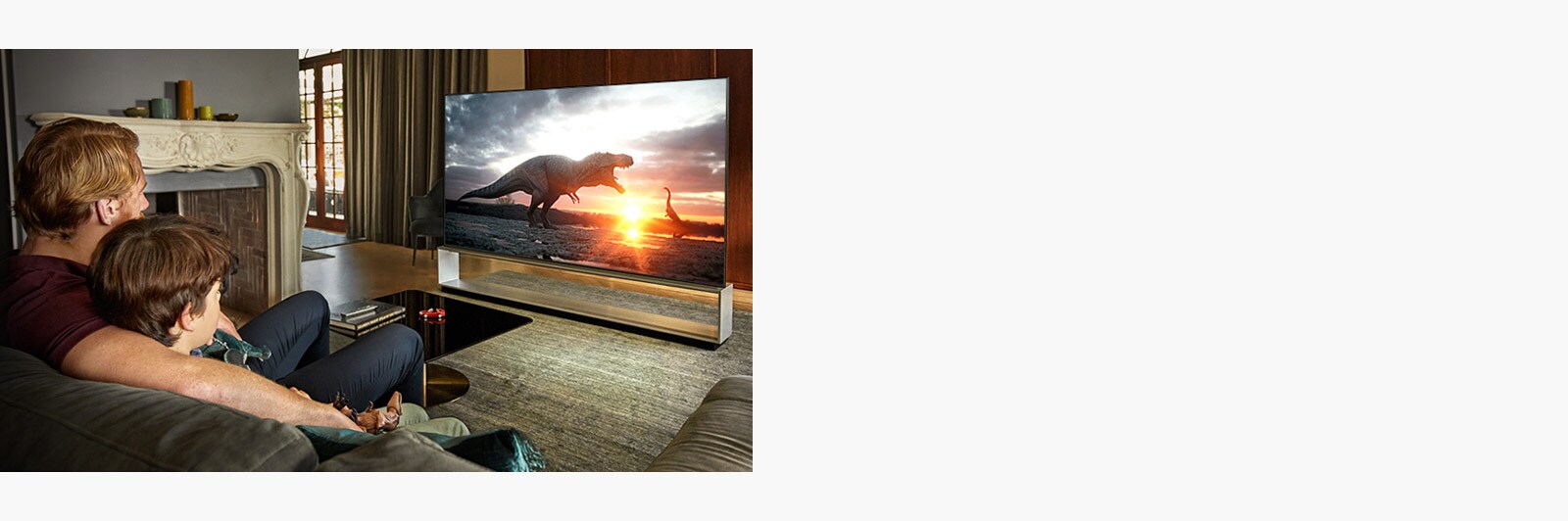 Tēvs un dēls lielā televizorā skatās dokumentālo filmu par dinozauriem