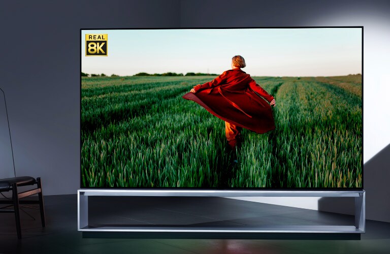 LG OLED 8K televizorā redzams reālistisks 8K attēls ar sievieti sarkanā trencī skrienam pa zaļojošu rīsu lauku