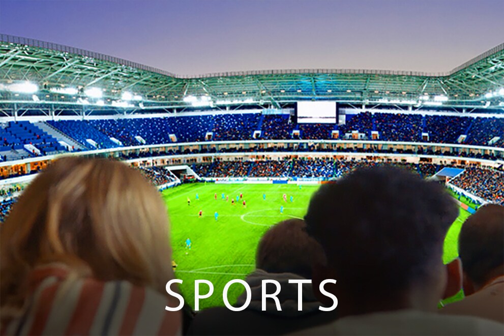 Cilvēki lielā televizorā skatās futbola spēli ar visu stadionu fonā