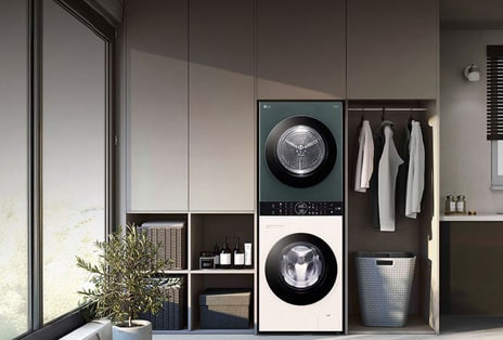 LG WashTower divās krāsās – tumši pelēku žāvētāju augšpusē un baltu veļas mazgājamo mašīnu apakšā, šaurā bēšā veļas telpā.
