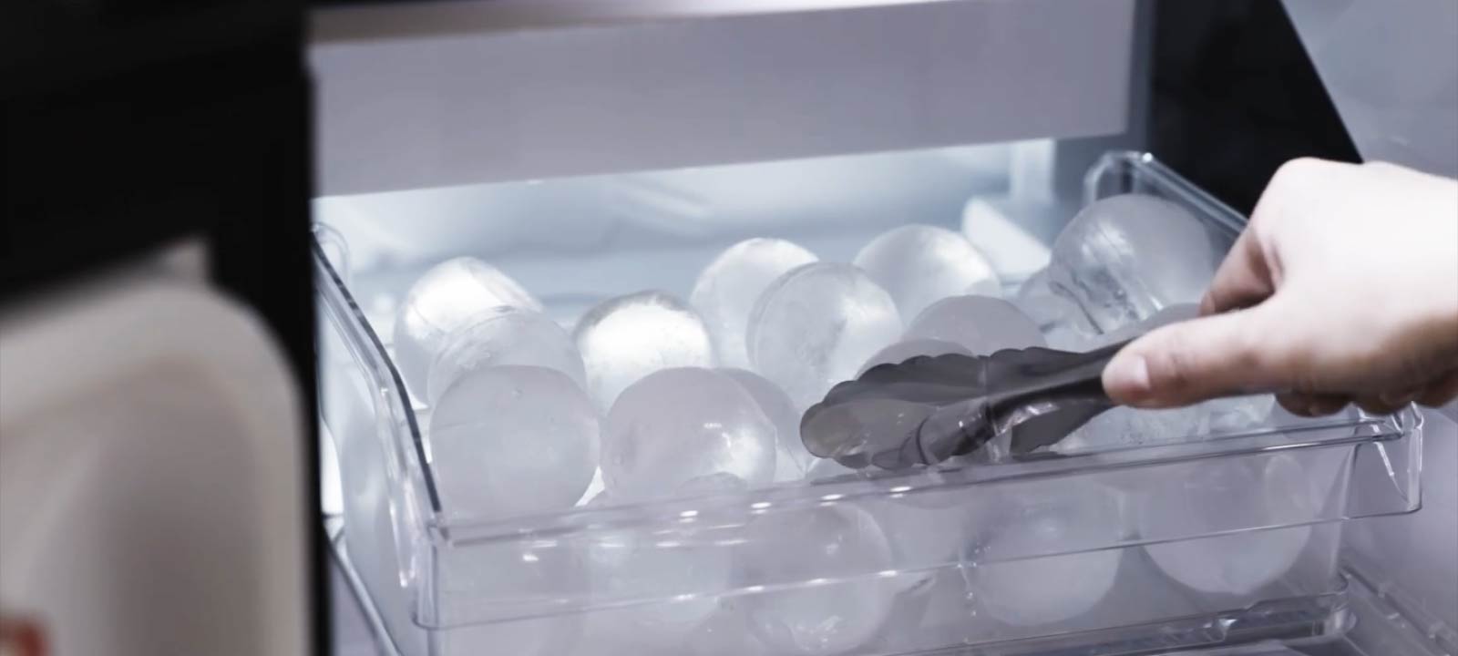 Knaibles paceļ apaļu ledus bumbu no caurspīdīgas paplātes saldētavā