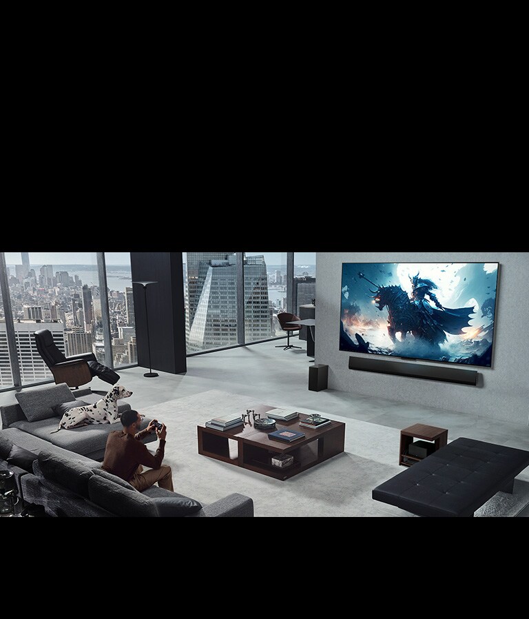 Dzīvojamā istaba ar vīrieti, spēlējot video spēli ar pie sienas piestiprinātu LG True Wireless TV un LG Soundbar. Vīrietim rokās ir kontrolieris, net spēļu konsole nav tieši redzama. Tāpat nav redzamu vadu. Zero Connect Box skaisti novietota zem sānu galdiņa un gandrīz nav saskatāma.