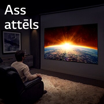 Tumšā telpā vīrietis sēž dīvānā un skatās televizoru, kurā redzama saule lecam aiz zemeslodes.