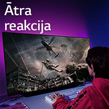 Meitene spēlē datorspēli lielā televizora ekrānā, kurā redzams, kā kareivis laižas lejup no helikoptera.