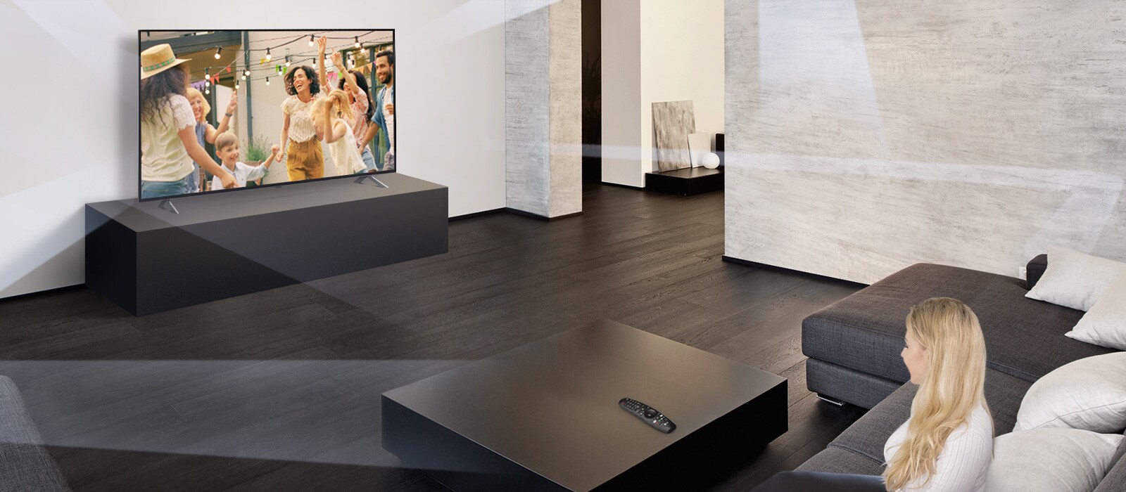 Sieviete lielā, minimālisma stilā veidotā viesistabā skatās, kā televizorā dejo cilvēki.