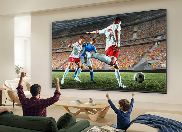 LG QNED evo AI QNED82 Mini LED Ultra Big TV rāda intensīvu, liela mēroga futbola spēli ar izsmalcinātu attēla kvalitāti un dzīvīgām krāsām, kamēr ģimene kopā skatās spēli no dīvāniem viesistabā.