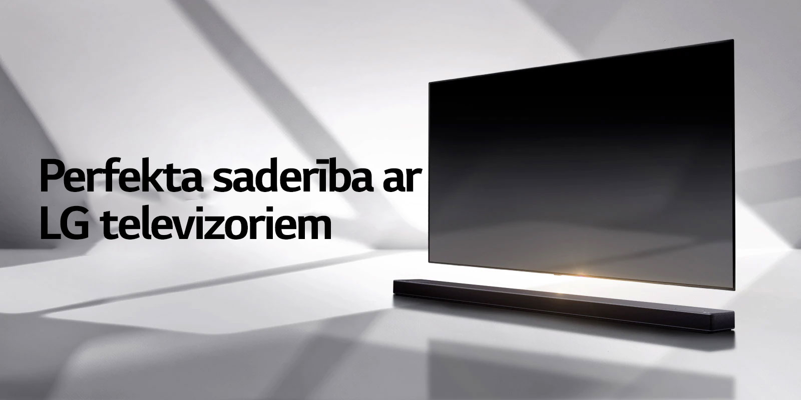 Skaņas josla un televizors novietoti uz baltas grīdas, un no ārpuses aiz tiem stiepjas ēna.