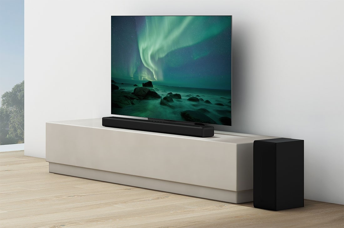 LG Soundbar S65Q, Baltā viesistabā zem televizora atrodas skaņas josla, tieši blakus ir redzams aizmugures skaļrunis., S65Q, thumbnail 5