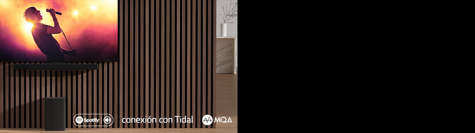 LG OLED C ir piestiprināts pie sienas, zem tā uz ekskluzīvā kronšteina ir piestiprināts LG Sound Bar SC9S. Zemo frekvenču pastiprinātājs ir novietots zem tā. TV ekrānā redzama koncerta aina.