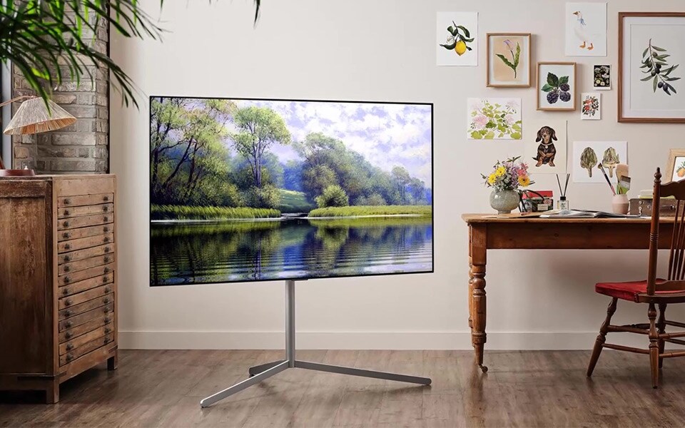 A picturesque lakeside image is shown on a standing OLED TV in an artistic home office.