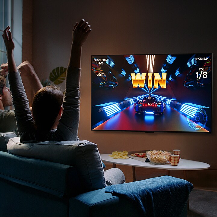Cilvēki spēlē LG OLED televizorā spēli ar vadības pulti.