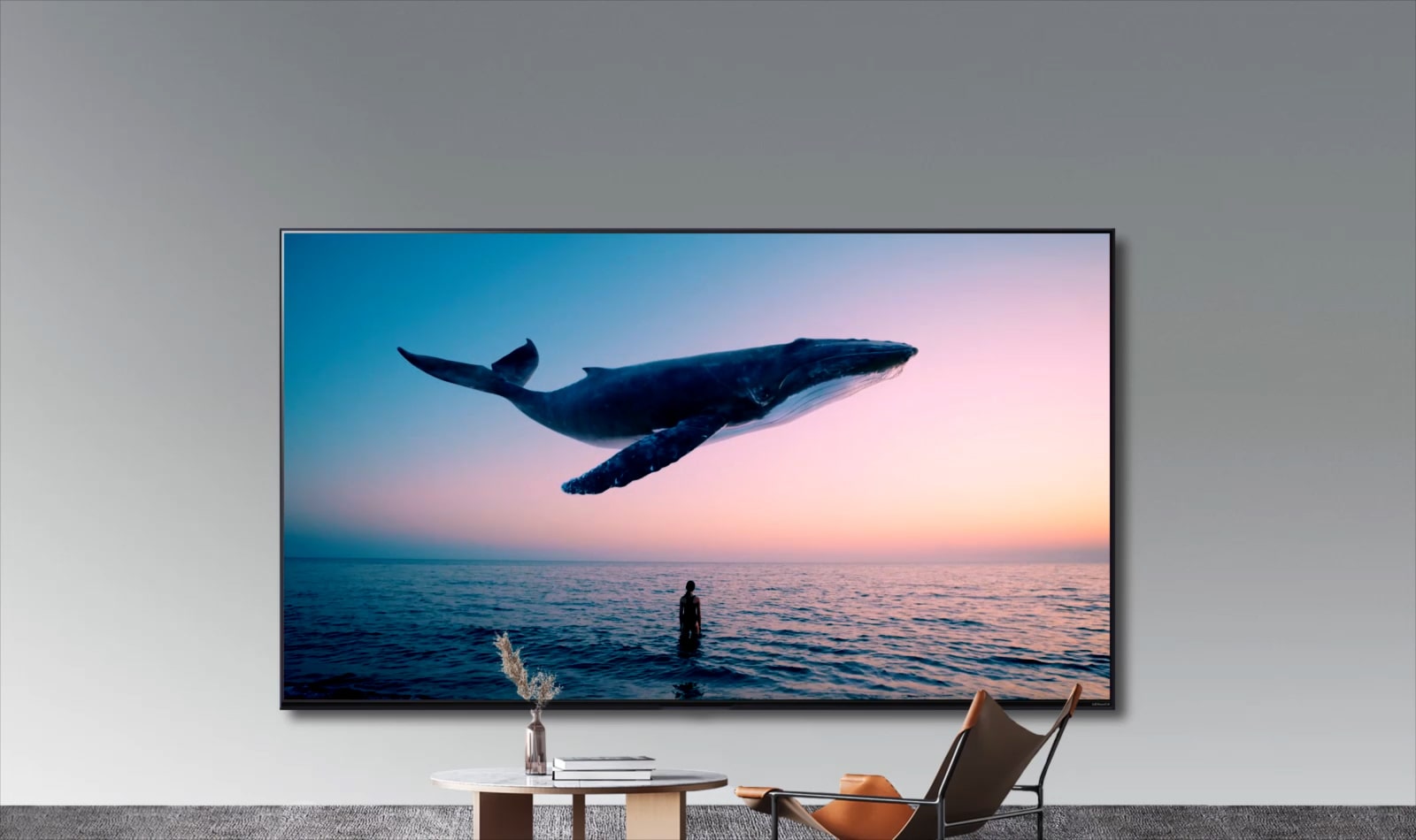Une énorme baleine et une femme apparaissent sur le téléviseur accroché au mur d’une pièce où se trouvent un simple canapé orange et une table ronde. 