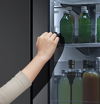 The front view of a black glass InstaView refrigerator with the light on inside. Hands tapping on InstaView screen.