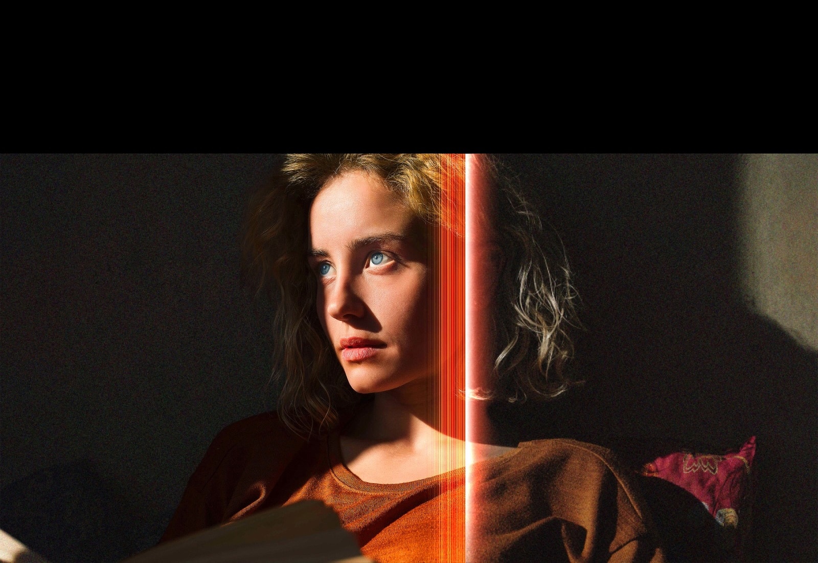 A woman with piercing blue eyes and a burnt orange top in a dark space. Red lines depicting AI refinements cover part of her face, which is bright and detailed, while the rest of the image looks dull. 