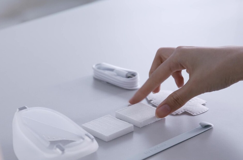 Wearable air purifier accessories are placed on the desk. A person is trying to pinch one of the PuriCare filters with her thumb and index finger.