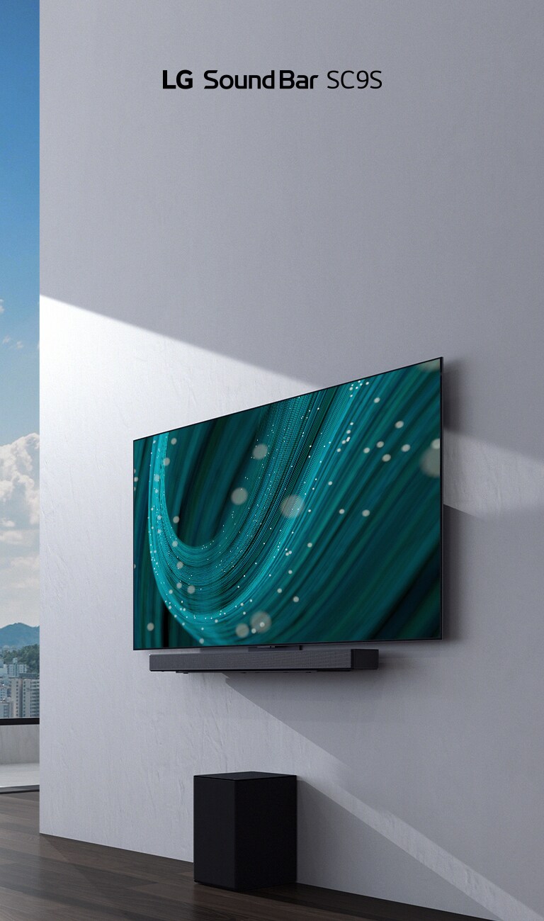 TV and LG Sound Bar SC9S are hung on a white wall. Below a black wireless subwoofer is placed on the floor. Beyond the window on the left a city view with the blue sky can be found.