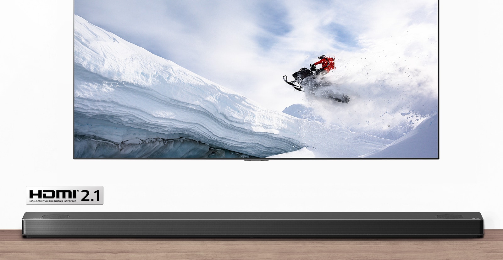 TV and Soundbar are seen from the front. TV shows man riding snowmobile in the snowy mountains. HDMI 2.1 logo is below TV. 