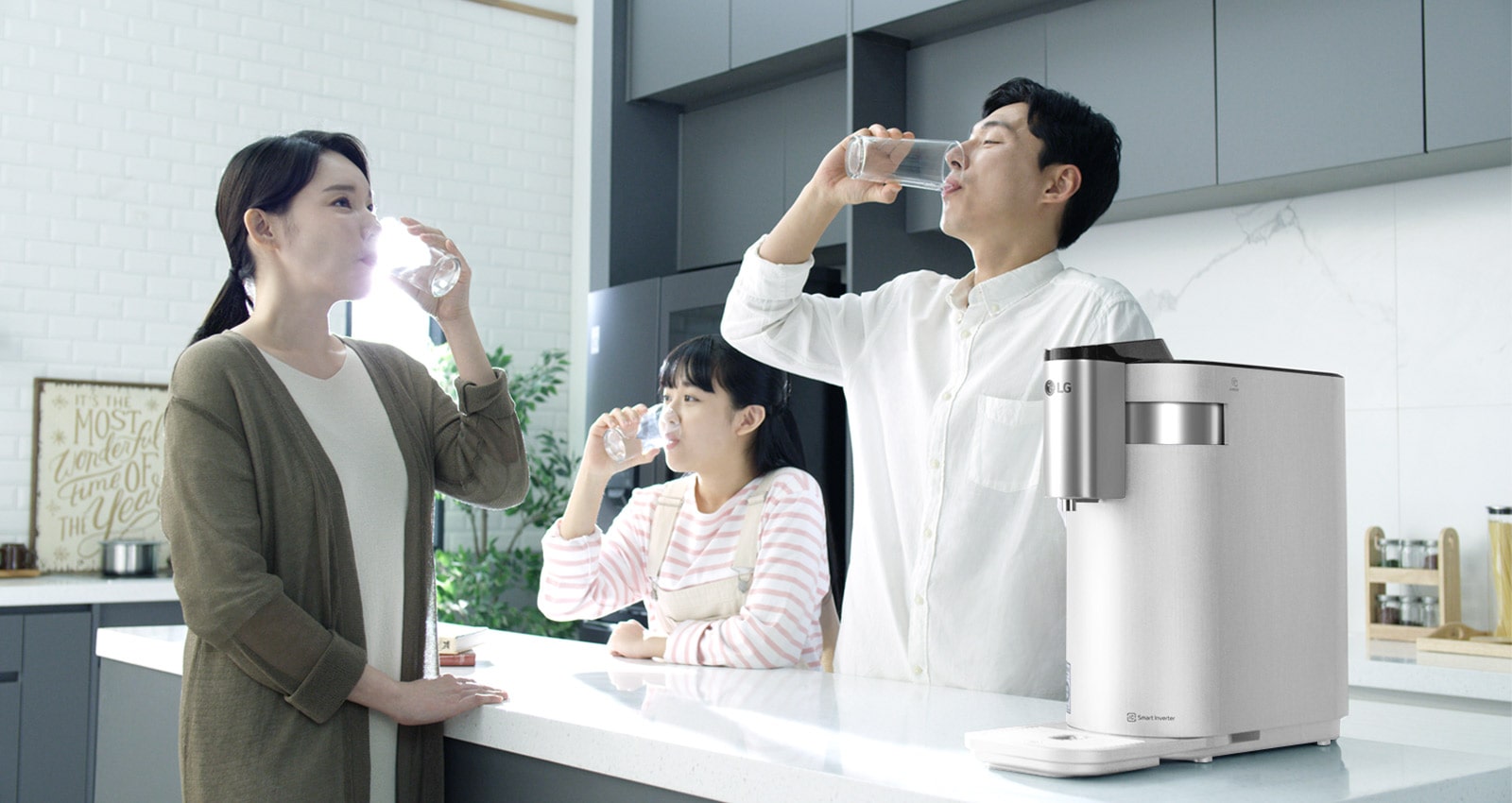 A family of three stand around a kitchen counter drinking water with the PuriCare Water Purifier on the counter in the foreground.