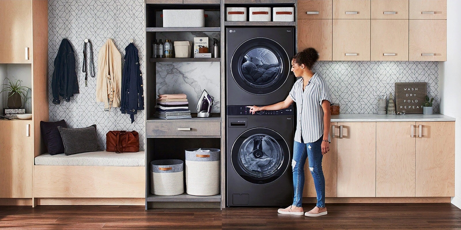 A black LG Wash Tower is installed in a laundry room and a woman stands to one side leaning in to press a button on the machine.