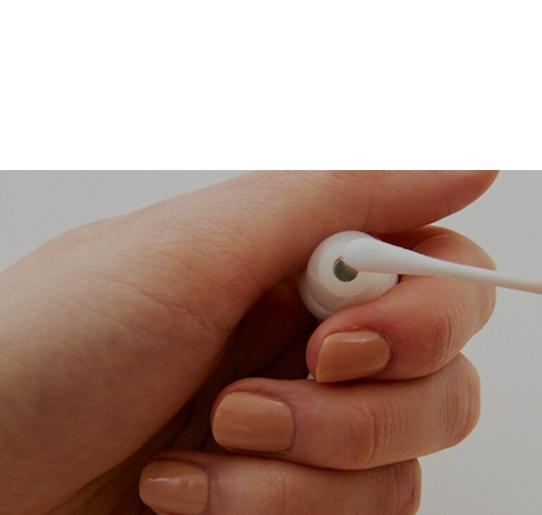 Een afbeelding van het in de hand houden van de oordopjes en het afvegen van de oordopjes met een wattenstaafje, waarmee de bacteriën in de oordopjes tot uitdrukking wordt gebracht.
