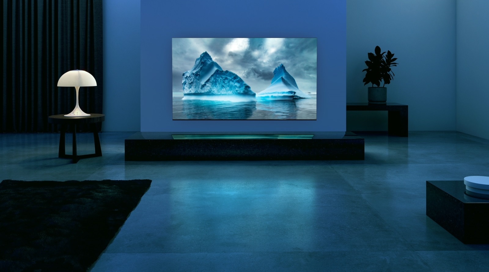 Een blauw neon circuit beweegt rond op blauw gletsjerbeeld. De camera zoomt uit en toont deze blauwe gletsjer op het TV-scherm. De tv is geplaatst in een brede woonkamer met een blauwe achtergrond. 