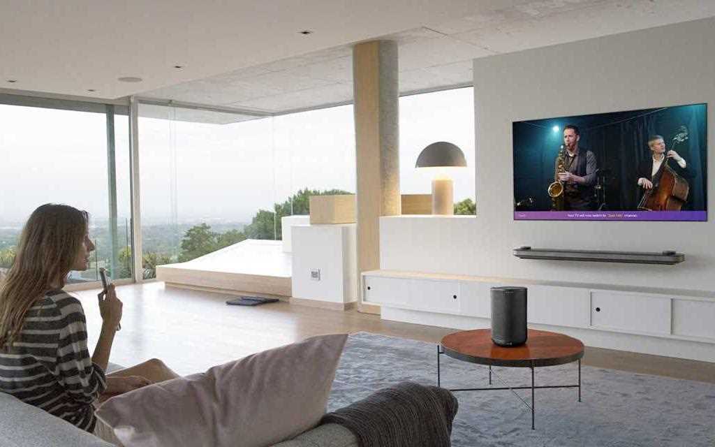 Een vrouw staat in de woonkamer, gebruikt de LG afstandsbediening om opdrachten te geven aan haar LG OLED Wallpaper TV. 