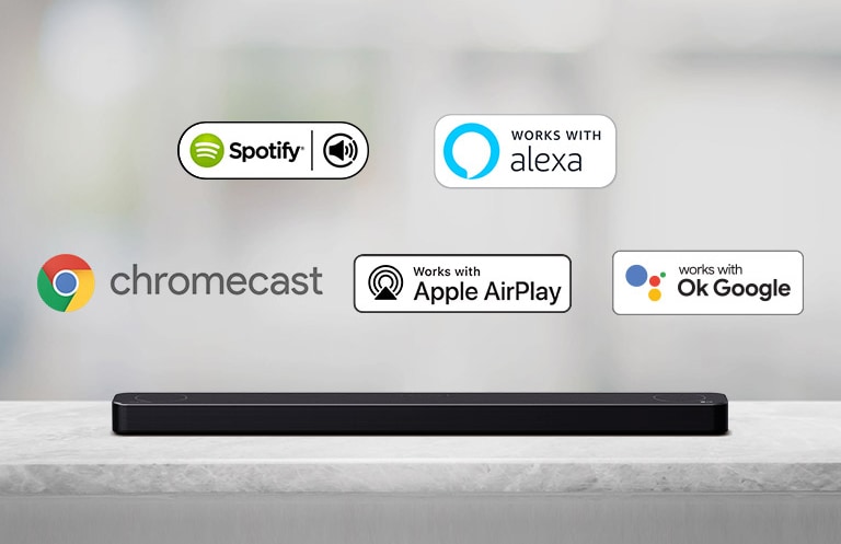Det er plassert en lydplanke på en grå hylle og det er AI plattform-logoer, og logoene Spotify, Alexa, Chromecast, Apple Airplay og deretter OK Google kommer inn fra venstre mot høyre.