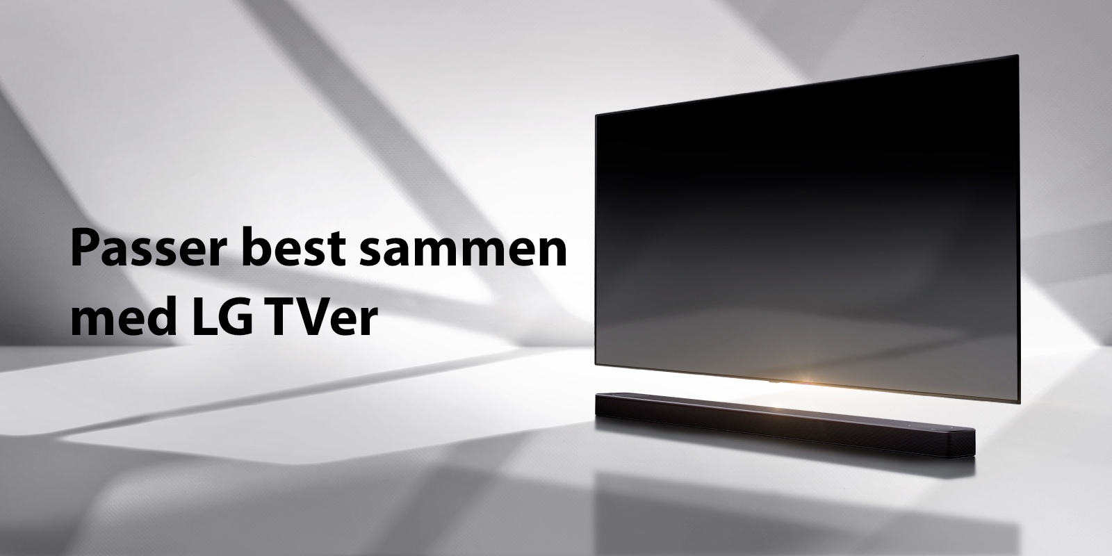 En lydplanke og en TV er plassert på et hvitt gulv og det er en skygge som kommer utenfra like bak.