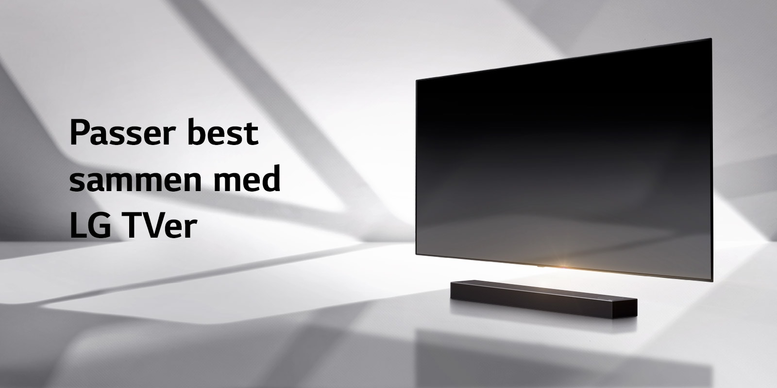 En lydplanke og en TV er plassert på et hvitt gulv og det er en skygge som kommer utenfra like bak.