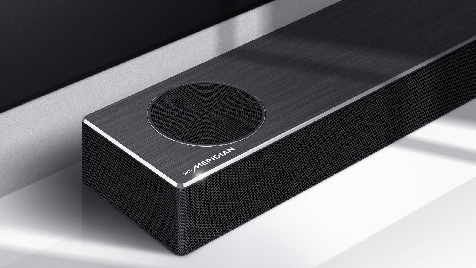 Nærbilde av LG Soundbars venstre side med Meridian-logoen vist på nedre venstre hjørne av produktet. Nedre venstre side av TVen er også synlig. 