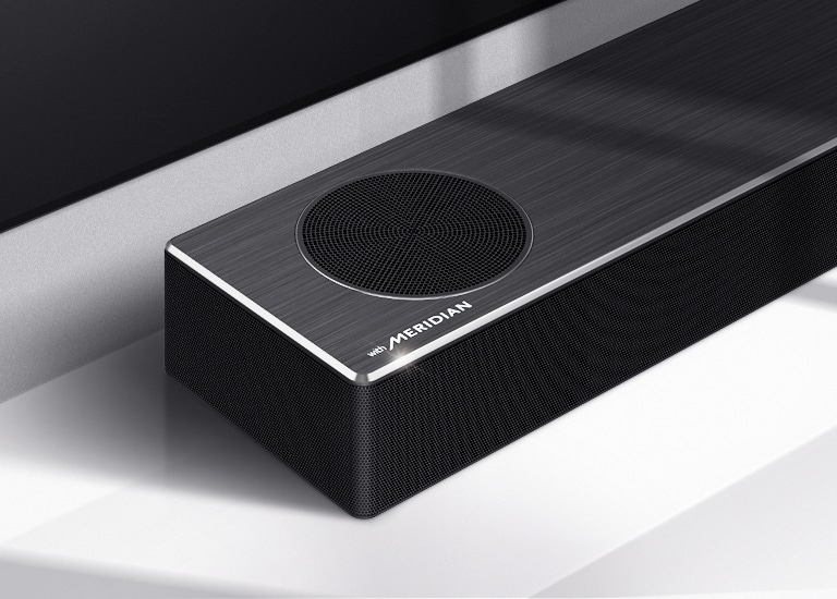 Nærbilde av LG Soundbars venstre side med Meridian-logoen vist på nedre venstre hjørne av produktet. Nedre venstre side av TVen er også synlig. 