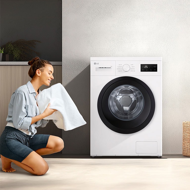 En kvinne som kneler foran en vaskemaskin i stuen og holder et rent teppe