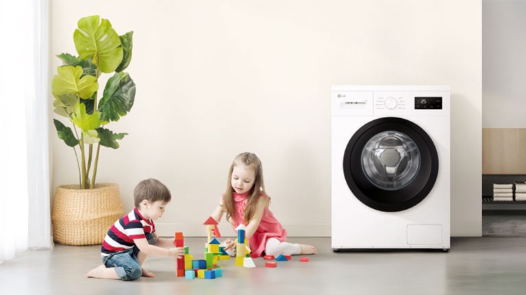 To barn som leker med fargerike klosser i nærheten av en vaskemaskin