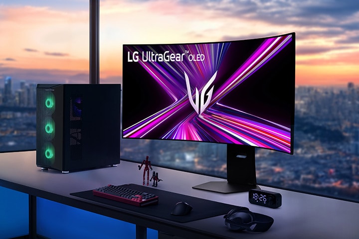 LG UltraGear OLED-skjerm på et spillbord med PC-oppsett, med utsikt over et bybilde ved solnedgang.