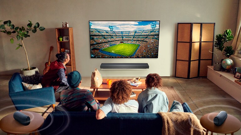 Folk ser på sport på TV i stua med Bluetooth-tilkoblede høyttalere bak