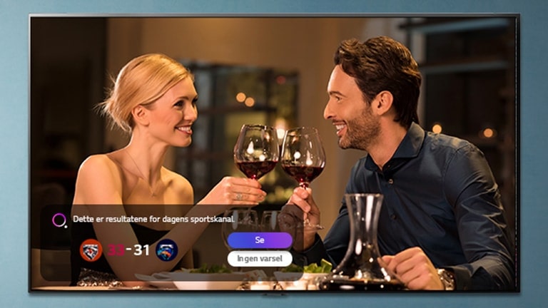 En mann og en kvinne klinker med glass på en TV-skjerm mens de blir varslet om sportsresultater