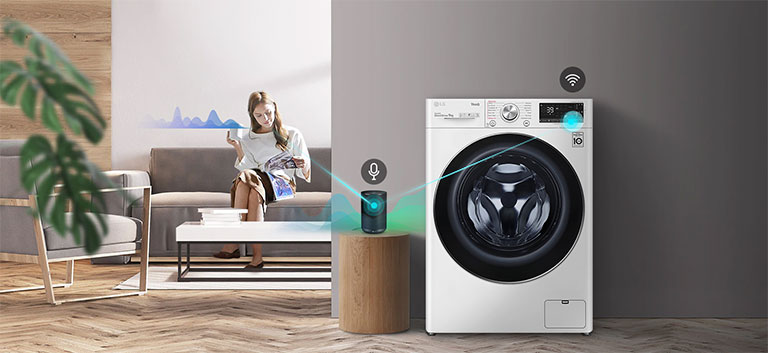 En kvinne som sitter på sofaen og drikker te og forteller hva vaskemaskinen skal gjøre gjennom AI-høyttaleren.