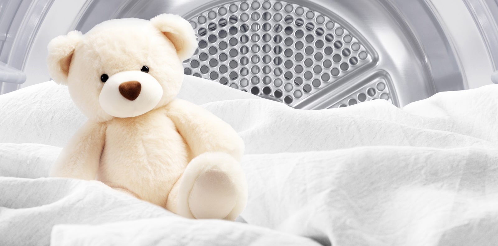 Bilde av en ren bamse og hvitt stoff inne i en tørketrommel.