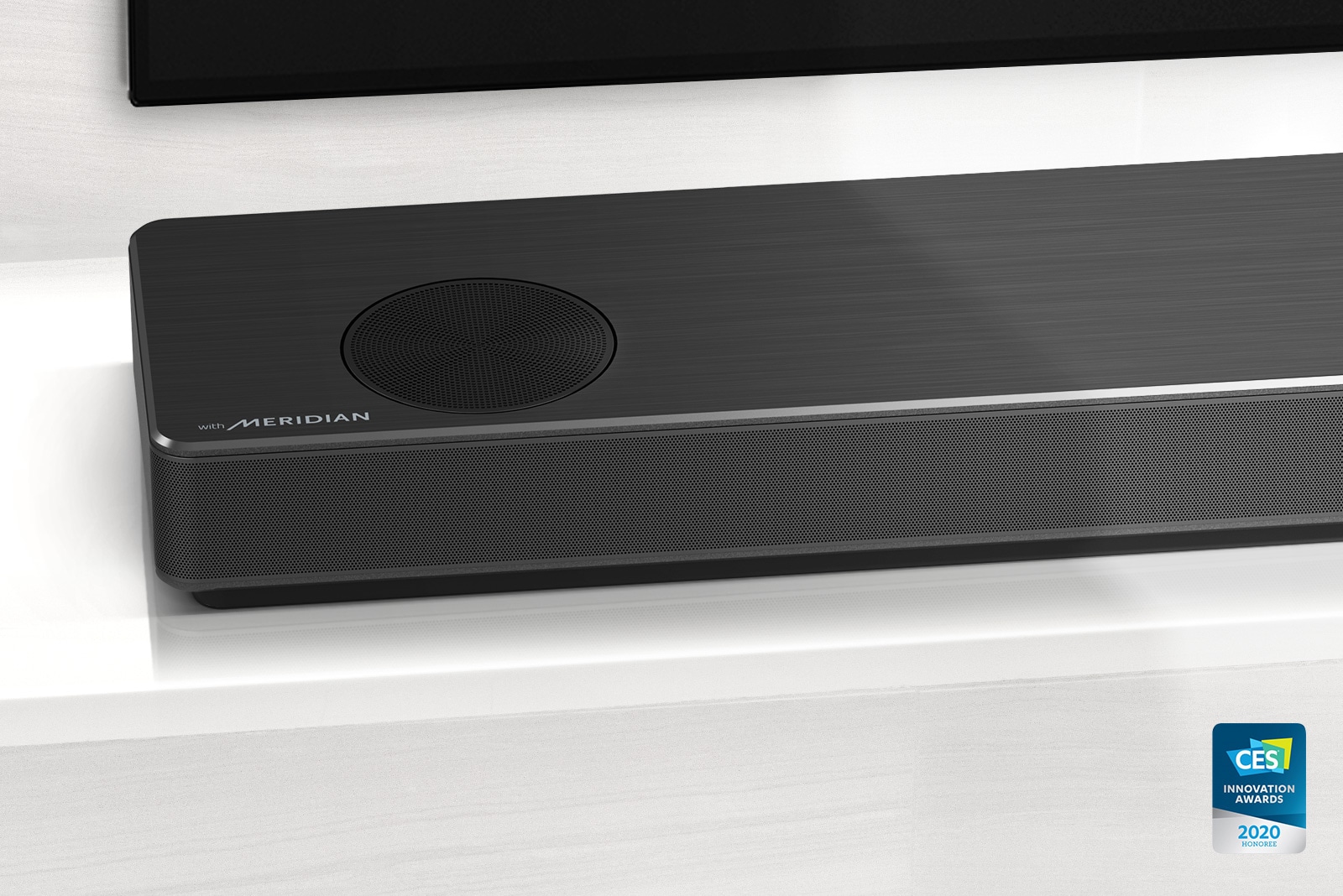 Close-up of LG Soundbar left side with Meridian logo shown on bottom left corner. Bottom left side of TV is also visible. 