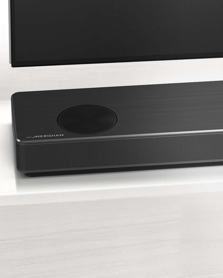 Nærbilde av LG Soundbars venstre side med Meridian-logoen vist på nedre venstre hjørne. Nedre venstre side av TVen er også synlig. 
