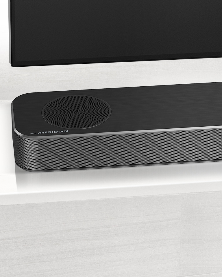 Nærbilde av LG Soundbars venstre side med Meridian-logoen vist på nedre venstre hjørne. Nedre venstre side av TVen er også synlig. 